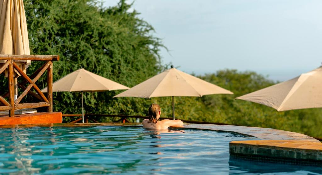 una donna in una piscina con ombrelloni di Escarpment Luxury Lodge Manyara a Mto wa Mbu
