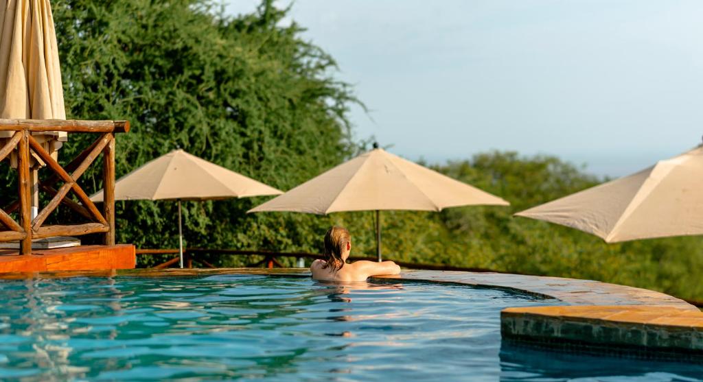 Eine Frau in einem Swimmingpool mit Sonnenschirmen in der Unterkunft Escarpment Luxury Lodge Manyara in Mto wa Mbu