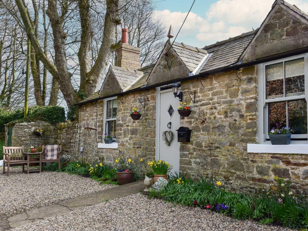 a stone cottage with a white door and a window at Fern Cottage in Bardon Mill