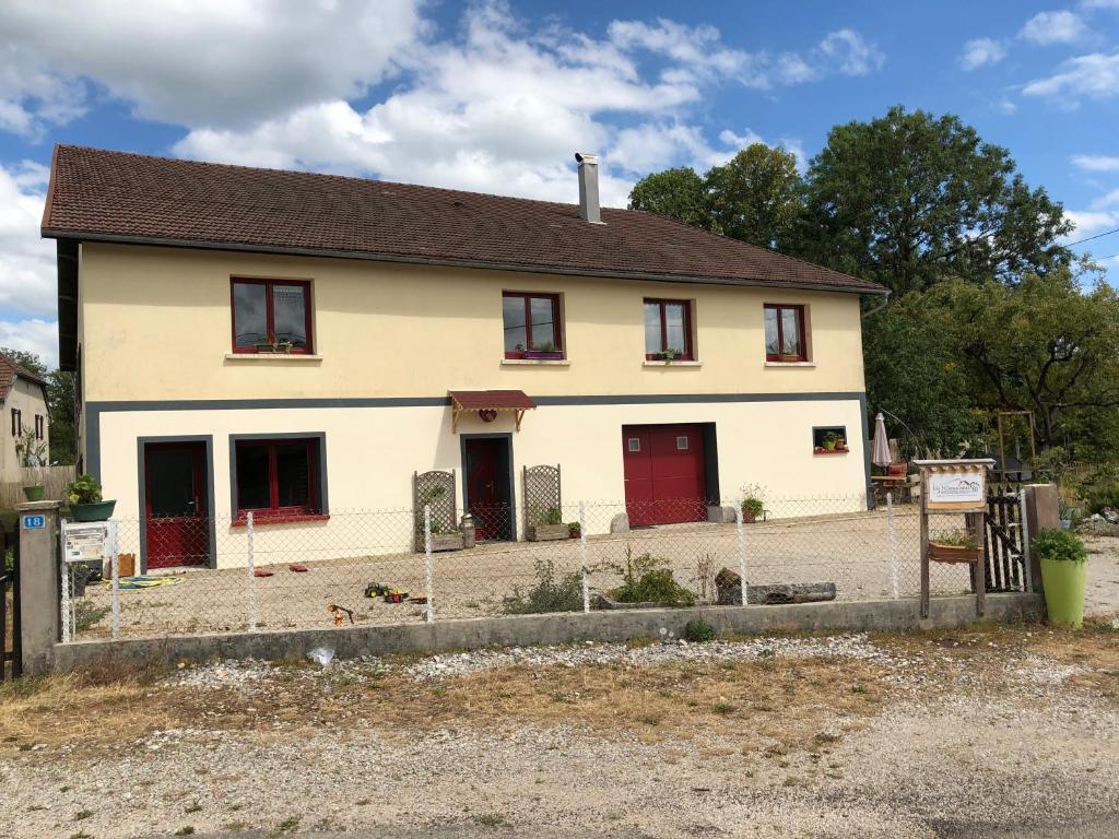 een wit huis met rode deuren en een tuin bij Les 3Crokignols, maison d’hôte familiale. in Saffloz