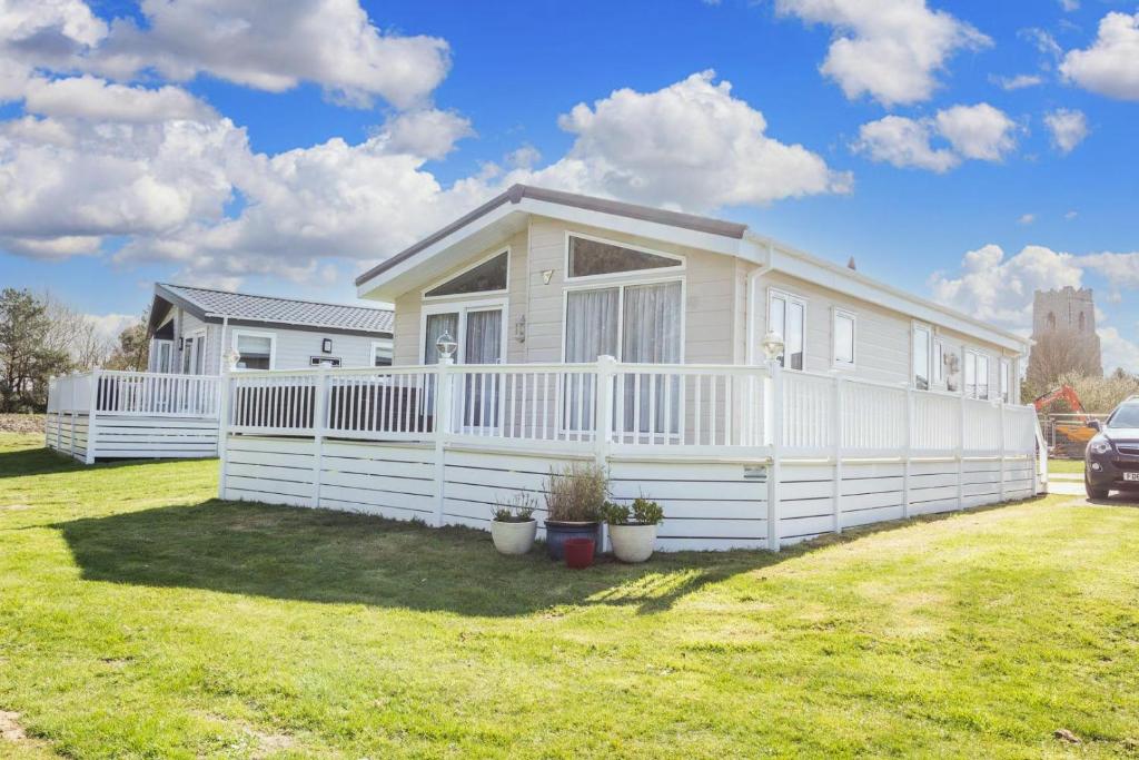a white house with a fence in a yard at Luxury 6 Berth Lodge With Wifi At Broadland Sands In Suffolk Ref 20011cv in Hopton on Sea