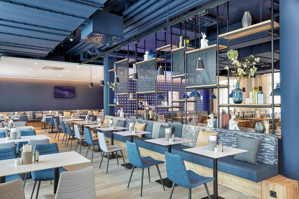 a restaurant with white tables and blue chairs at H2 Hotel München Olympiapark in Munich