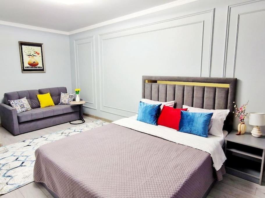 sypialnia z łóżkiem z kolorowymi poduszkami i kanapą w obiekcie НОВАЯ - 1 комнатная квартира! w mieście Taraz