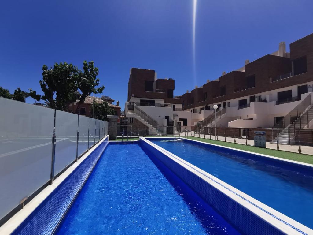 una piscina de agua azul frente a los edificios en Beach house los alcazares, en Los Alcázares
