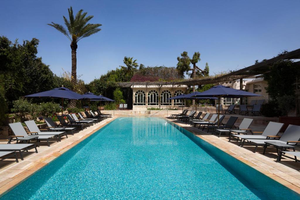 a swimming pool with lounge chairs and umbrellas at The American Colony Hotel - Small Luxury Hotels of the World in Jerusalem