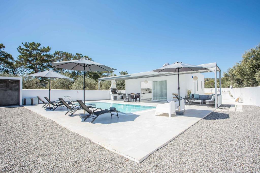 a swimming pool with umbrellas and chairs and a patio at VillaPhysis with Private Pool in Lardos