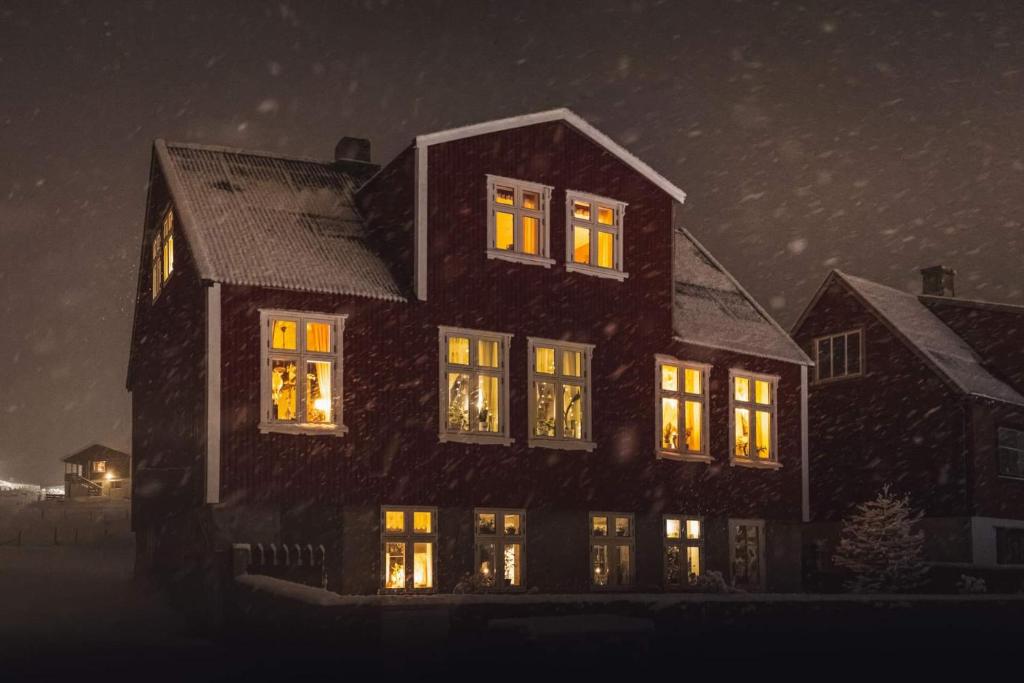 een groot huis met 's nachts verlichting in de ramen bij Heima í Stovu in Hvalba