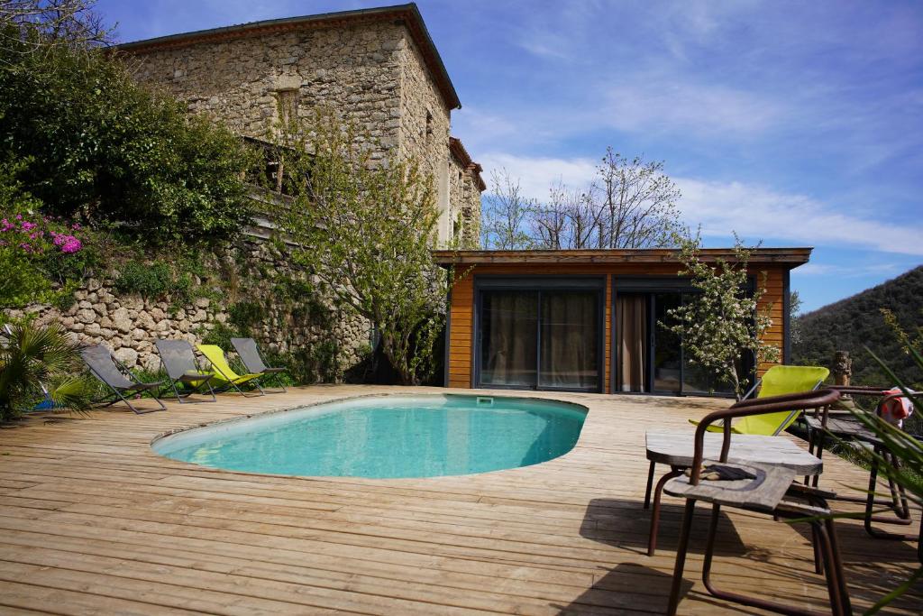 uma piscina num deque de madeira com cadeiras e uma casa em Mas Montet chez Raphael em Valleraugue
