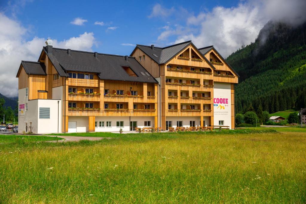 a large building with a grass field in front of it at COOEE alpin Hotel Dachstein in Gosau