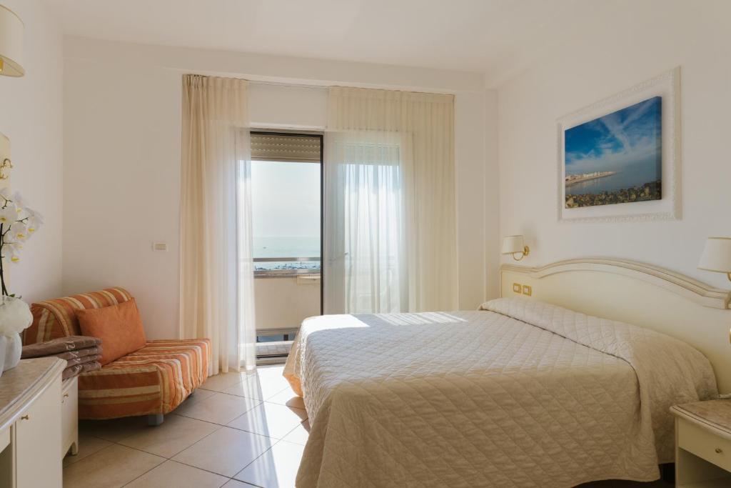 a bedroom with a bed and a chair and a window at Hotel Acapulco in Milano Marittima