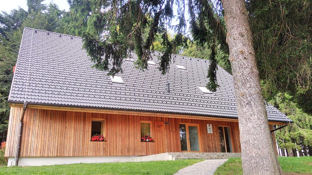 a wooden house with red flowers in front of it at Čandrova koča in Pohorje