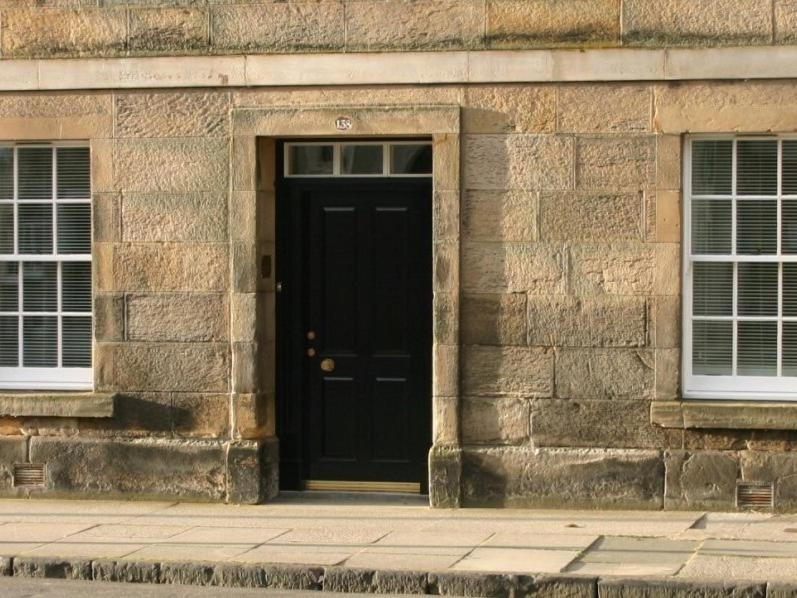 a black door on a stone building with two windows at 138 North Street - luxury 2 bed 2 bath with secret garden, summerhouse, putting green in St Andrews