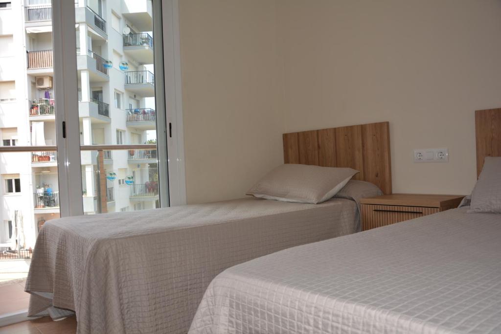 two beds in a room with a large window at APCOSTAS Villa de Madrid in Blanes