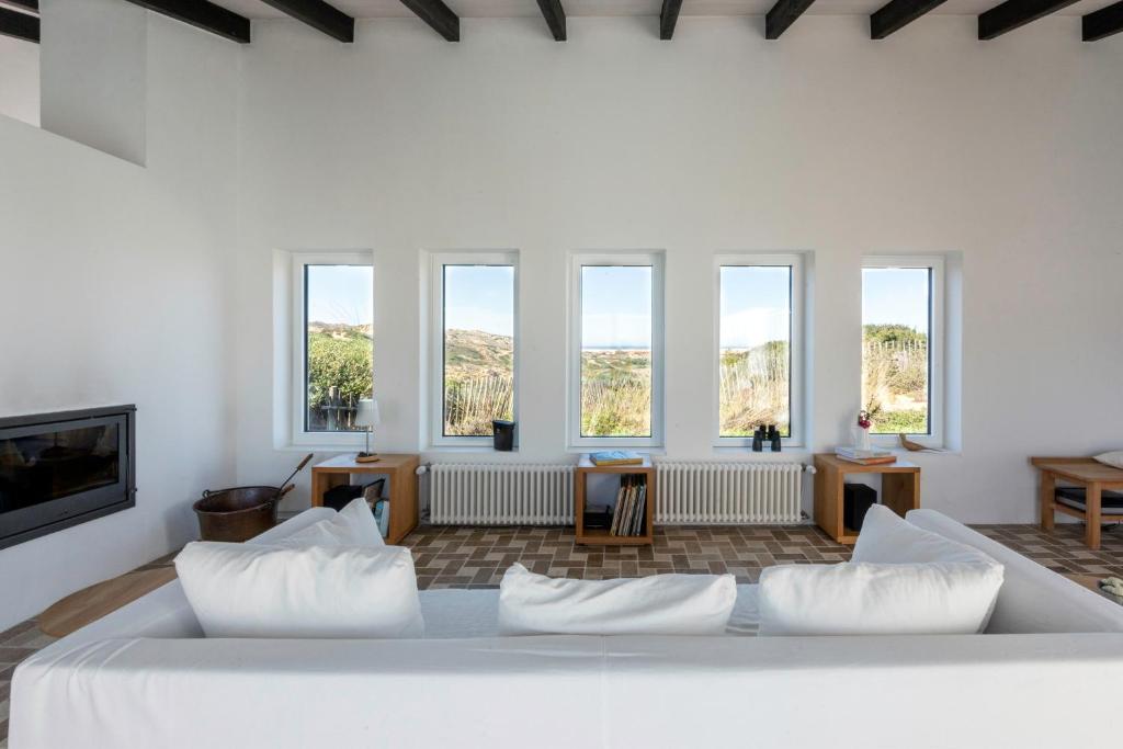 een wit bed met kussens in een kamer met ramen bij Sanderling beach & dune house in Carrapateira