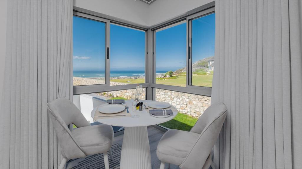 uma mesa branca e cadeiras num quarto com janelas em Cliff Haven em Struisbaai