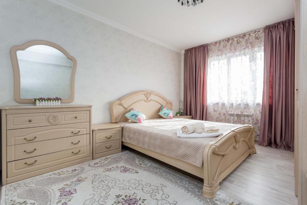 a bedroom with a bed with a dresser and a mirror at Светлая квартира рядом с парком Горького in Almaty