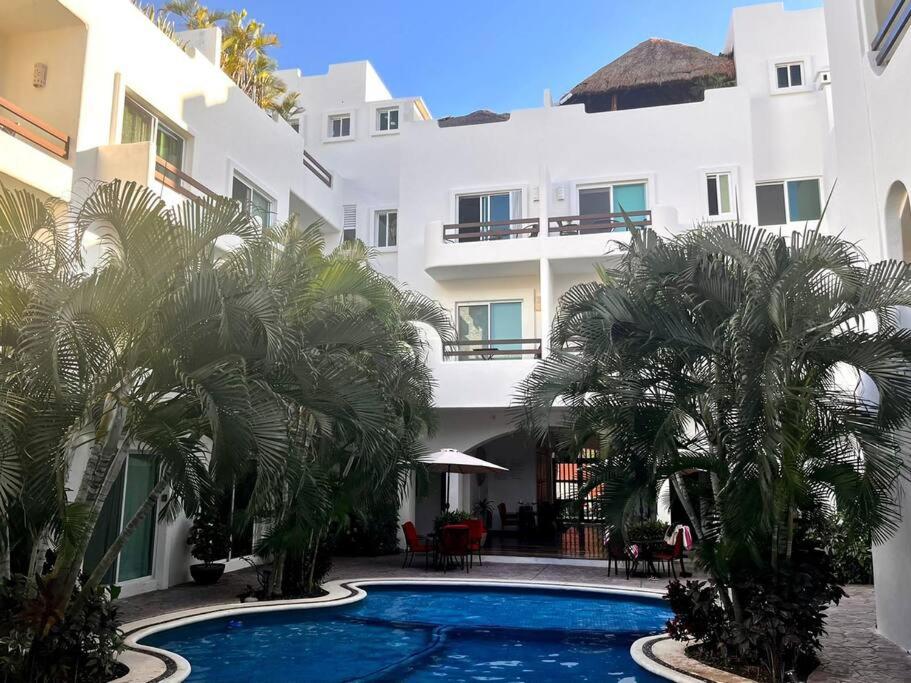 a swimming pool in front of a building with palm trees at Playakaan21 by Utopia in Playa del Carmen