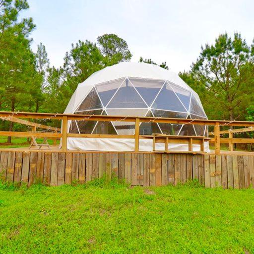 une grande tente dans un champ derrière une clôture en bois dans l'établissement The Pines, Glamping Dome, 
