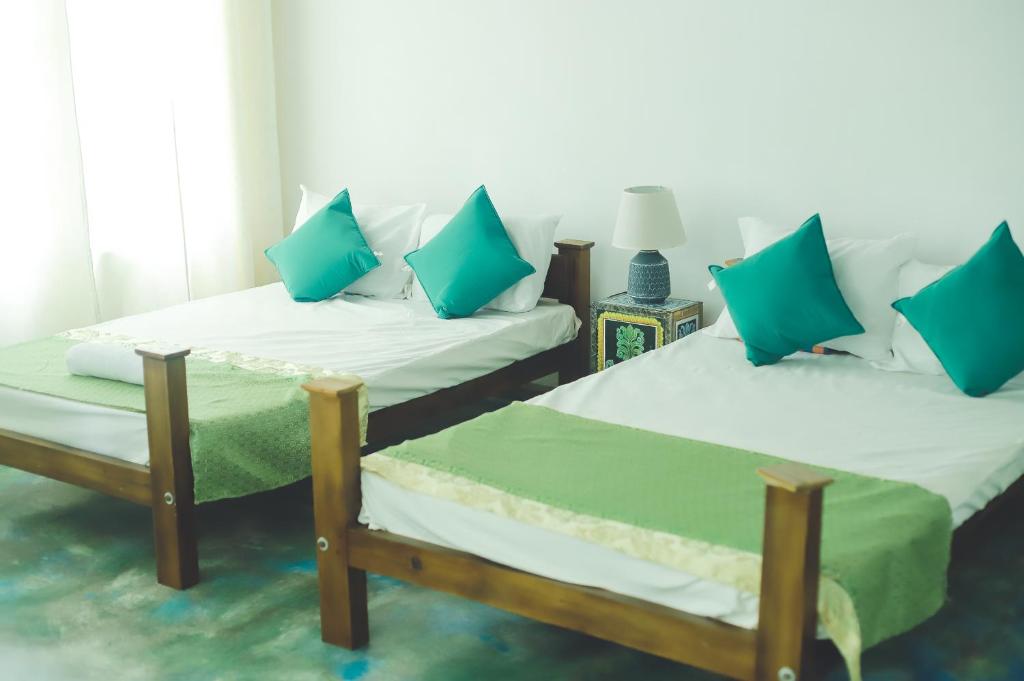 Duas camas num quarto com almofadas azuis e verdes em Barefoot Inn Kandy em Kandy