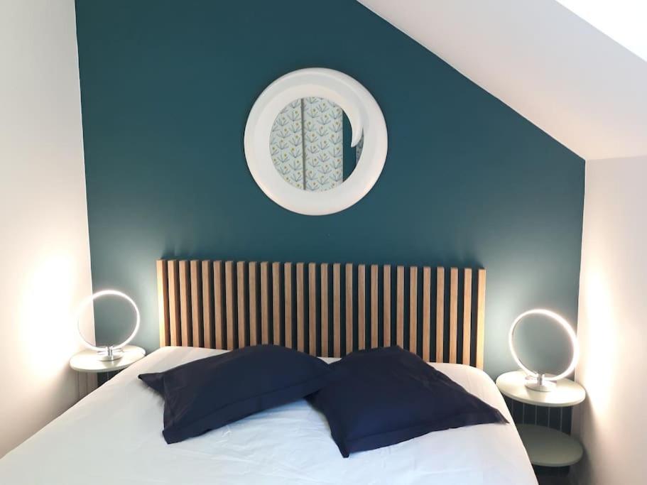 1 dormitorio con pared azul, cama y espejo en Les cottages du golf à Ploemel, en Ploemel