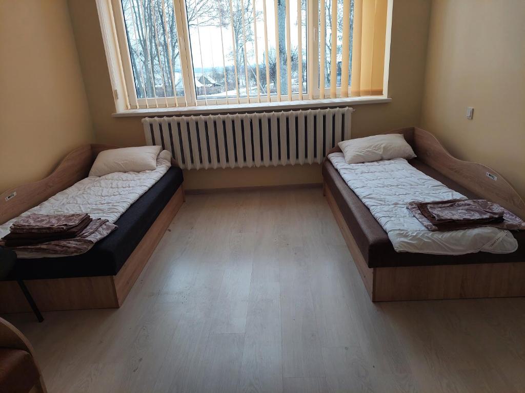 two beds in a room with a window at Kriaunų bendruomenės Svečių namai in Gipenai