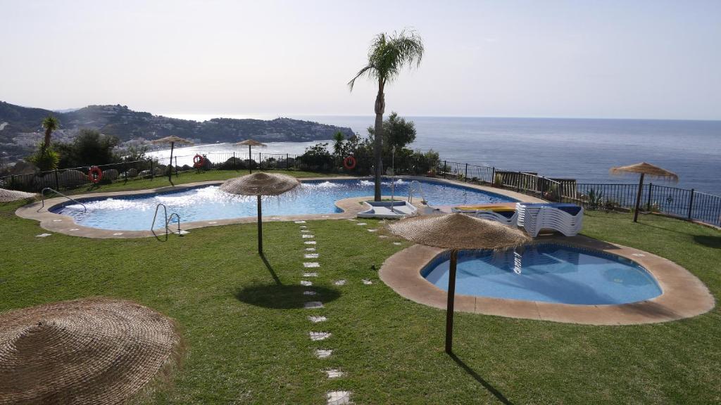 a swimming pool with straw umbrellas and the ocean at Casa del Mar in La Herradura
