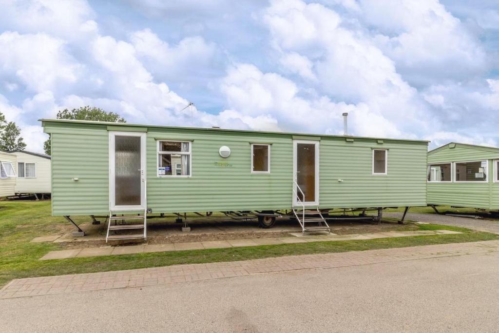 a green trailer with two folding chairs in a parking lot at 8 Berth Caravan At California Cliffs Holiday Park In Norfolk Ref 50007d in Great Yarmouth