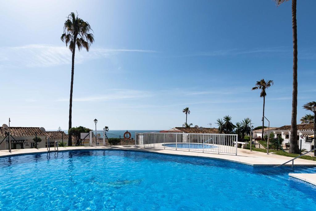 een groot zwembad met palmbomen en de oceaan bij CASA NOAH a 250m de la playa NUEVO in La Cala de Mijas