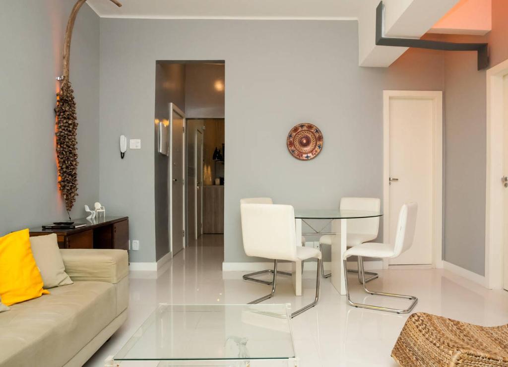 Leblon Dream Apartment في ريو دي جانيرو: غرفة معيشة مع طاولة زجاجية وكراسي بيضاء
