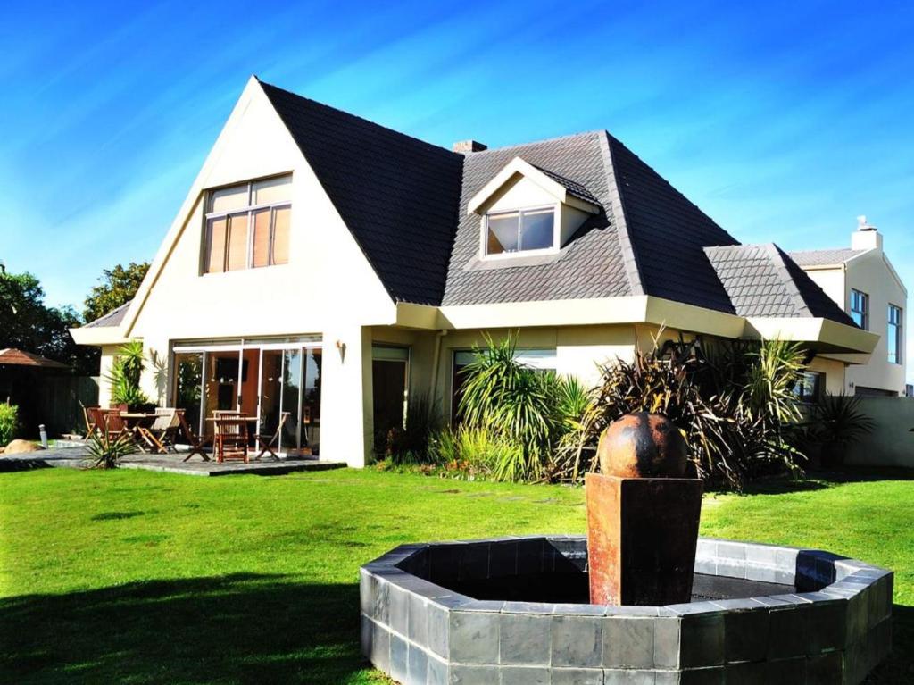 a white house with a black roof and a fountain at Mandalay Beach Guest House in Bloubergstrand