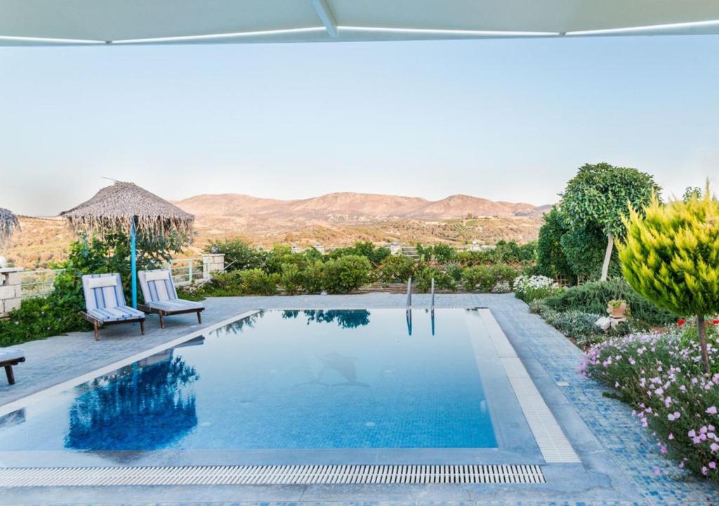 a swimming pool with two chairs and a umbrella at Zeus's Daughtes Villas in Pitsidia