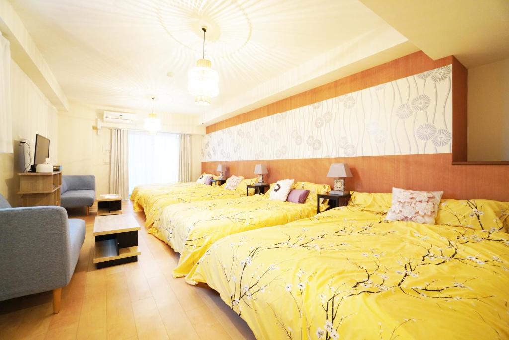 a hotel room with three beds with yellow sheets at MATATABI STAY Daikokucho in Osaka