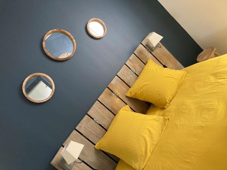 uma cama com almofadas amarelas e espelhos numa parede em la petite terrasse d’Arthur; appartement terrasse à 50m de la mer em Le Portel