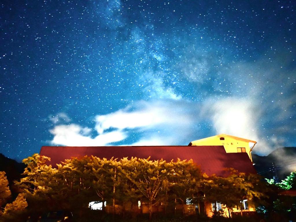 un edificio sotto un cielo stellato con alberi in primo piano di 筋肉と自然と遊ぶ宿 田島館 a Takayama