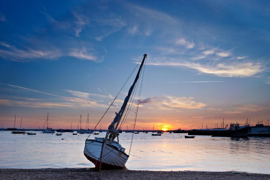 a sail boat sitting on the beach at sunset at Lighthouse Holiday Retreat in West Mersea