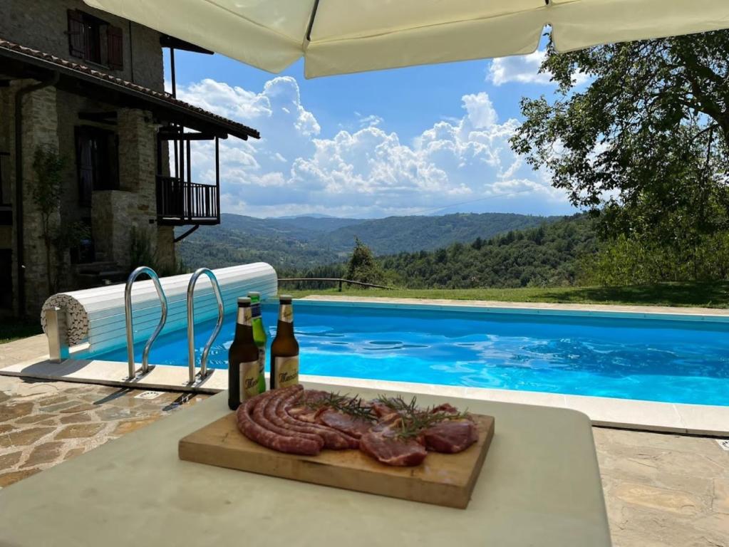 een tafel met twee flessen wijn en vlees naast een zwembad bij Cascina Manzoni appartamenti in Bossolasco