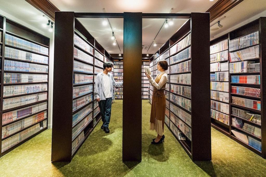 un hombre y una mujer caminando por una biblioteca en Relief Kokura ANNEX Book & Stay, en Kitakyushu