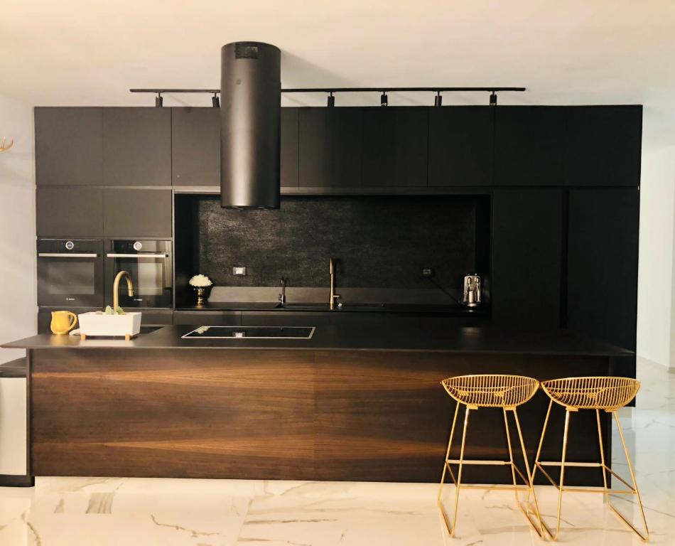 una cocina con armarios negros, fregadero y 2 sillas en Boutique Penthouse by Weizmann - פנטהאוס בוטיק, en Rechovot