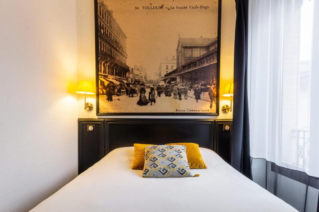 a bed in a room with a picture on the wall at Hôtel de France in Toulouse