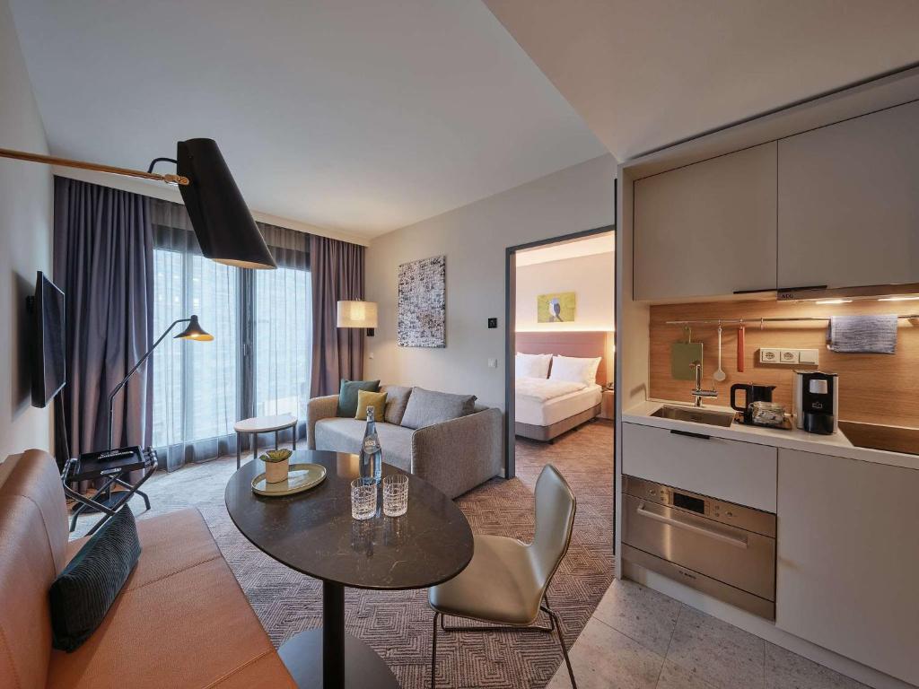 ケルンにあるAdina Apartment Hotel Cologneのキッチン、リビングルーム(テーブル付)が備わります。