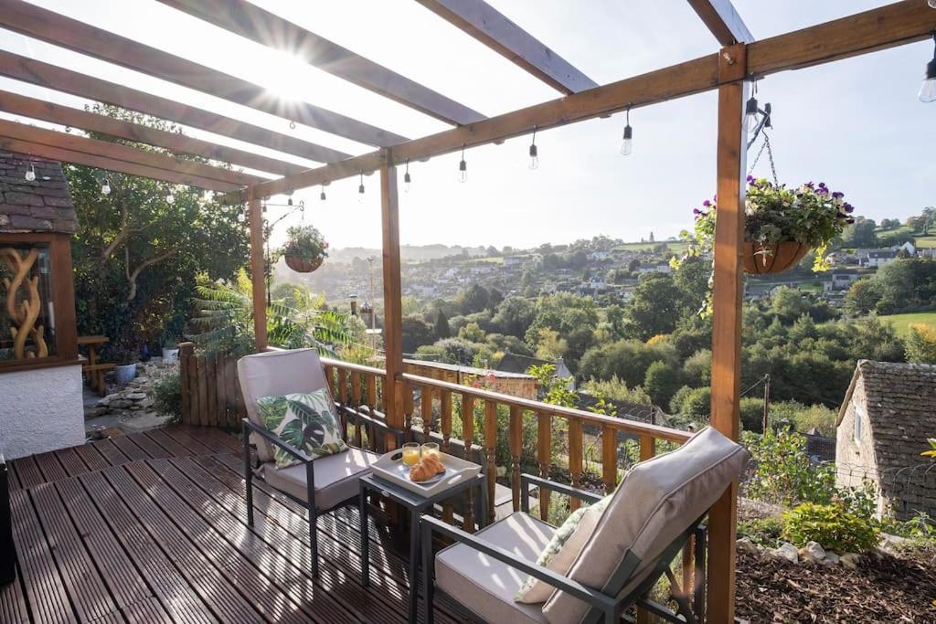 a wooden deck with two chairs and a table on it at Cosy Country Cottage with Stunning Views in Nailsworth in Nailsworth