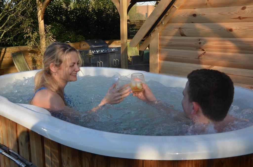 un hombre y una mujer en una bañera con una bebida en Stamford Meadows Glamping with Private Hot Tubs, en Stamford