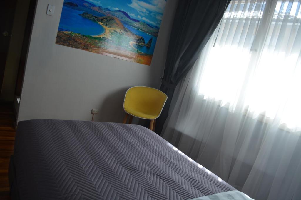 een slaapkamer met een bed met een gele stoel en een raam bij Blue house La Floresta in Quito