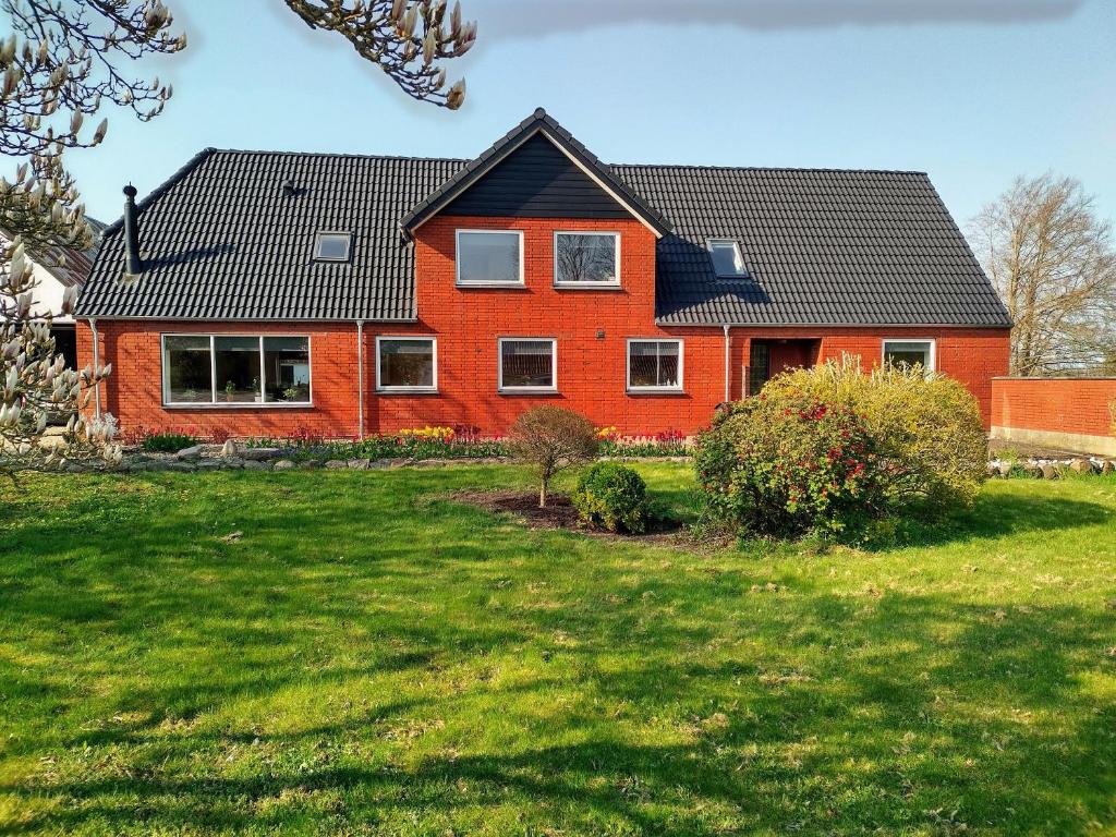 una casa roja con techo negro en un patio verde en Ferielejlighed Skovby ved Bogense, en Bogense