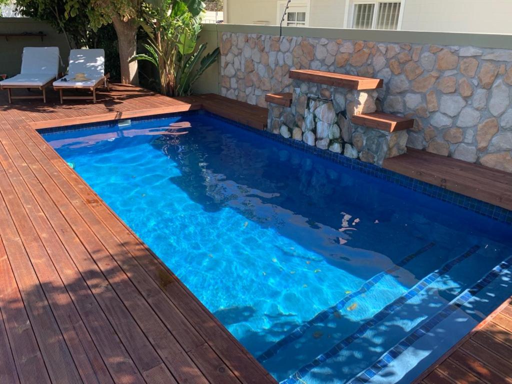 a pool with a wooden deck and a swimming pool with a stone wall at SOLAR POWERED - Heart of Constantia2 in Cape Town