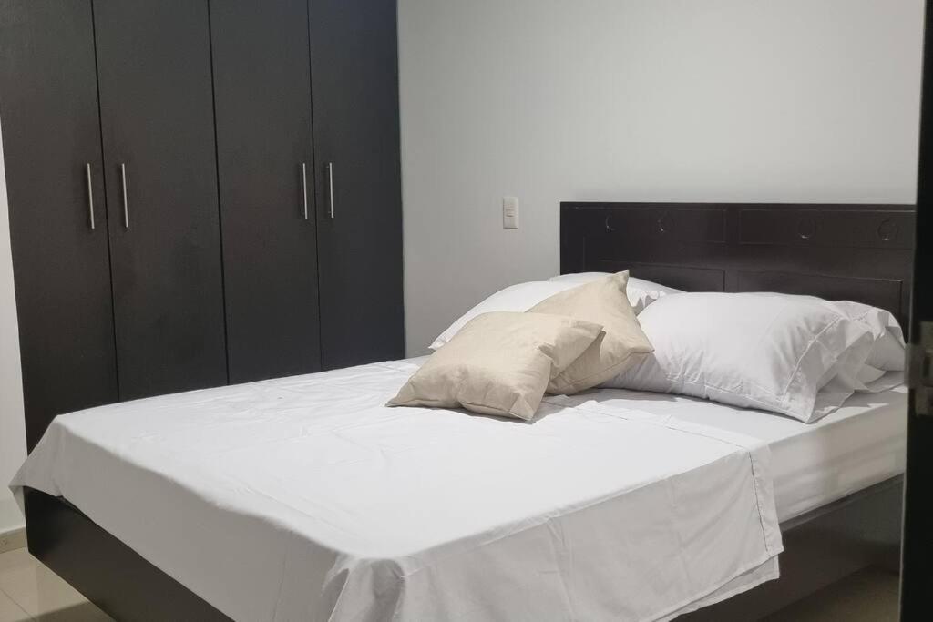 uma cama grande com lençóis brancos e almofadas em Soniella apto - WAIWA HOST em Bucaramanga