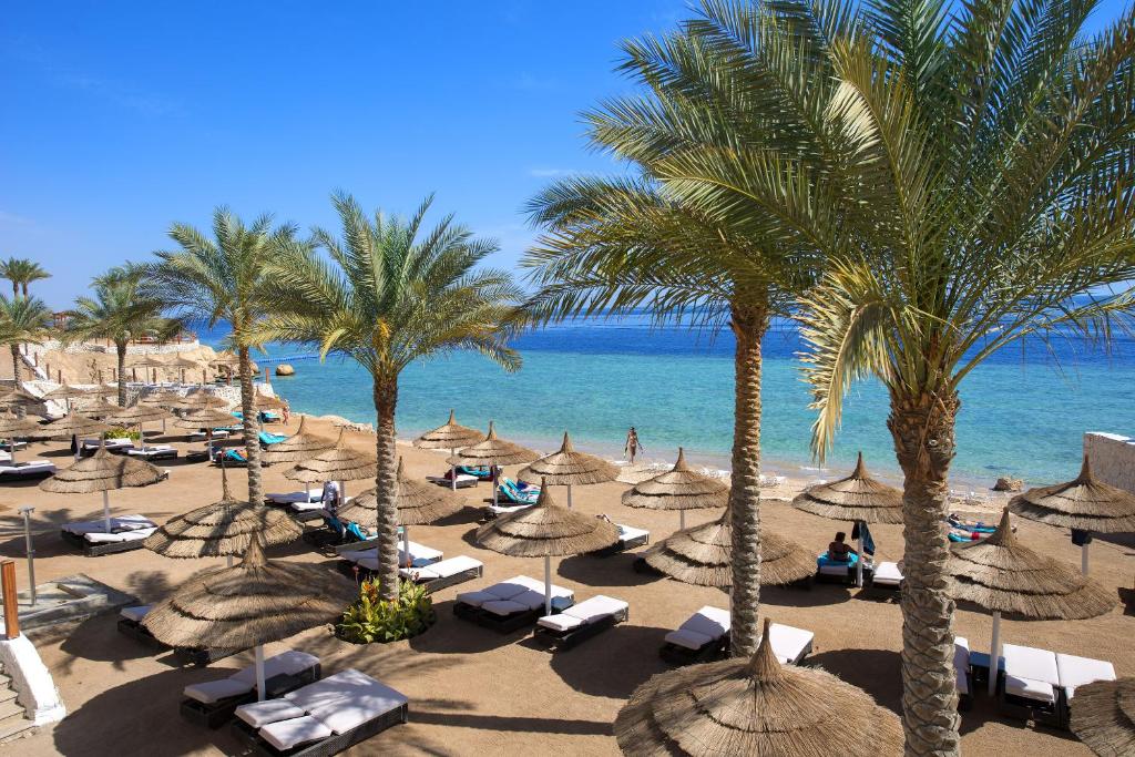 einen Strand mit Sonnenschirmen, Palmen und dem Meer in der Unterkunft Sunrise Montemare Resort -Grand Select in Sharm El Sheikh