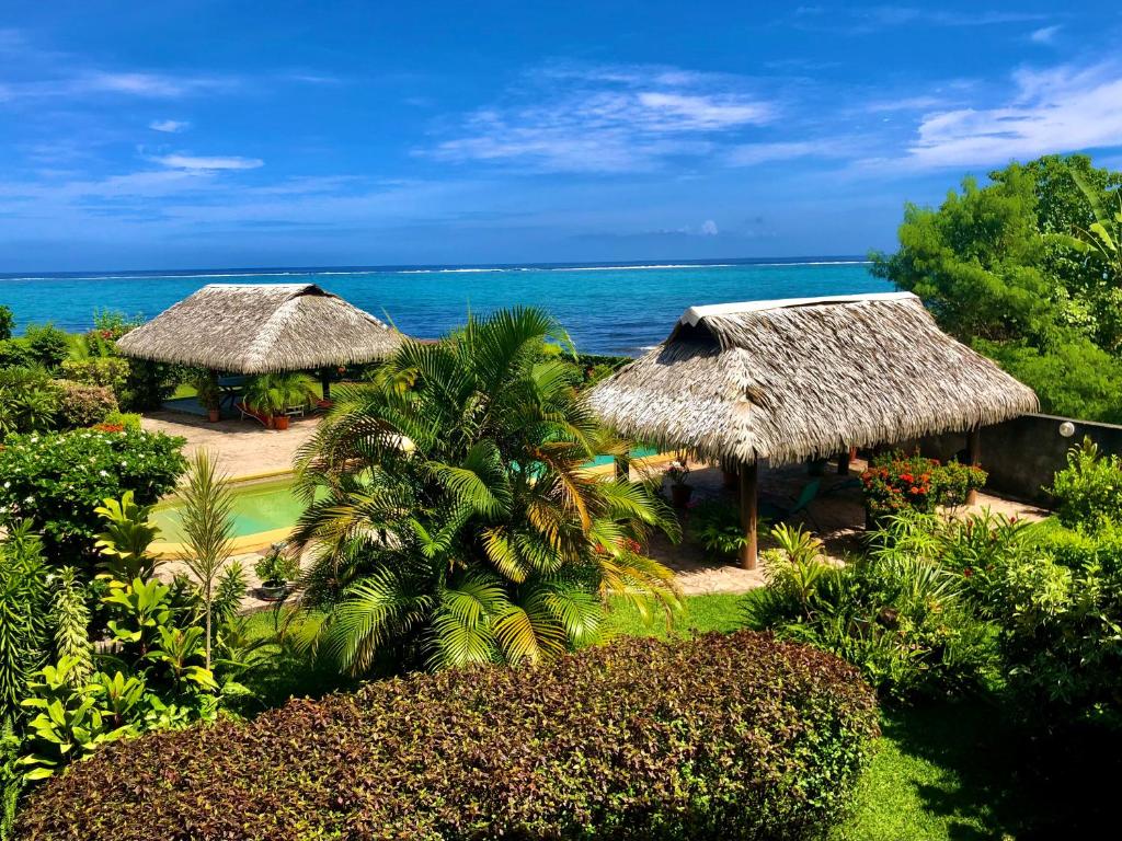 un complejo con 2 cabañas con techo de paja y el océano en Superbe bord de mer, accès lagon et piscine privée en Paea