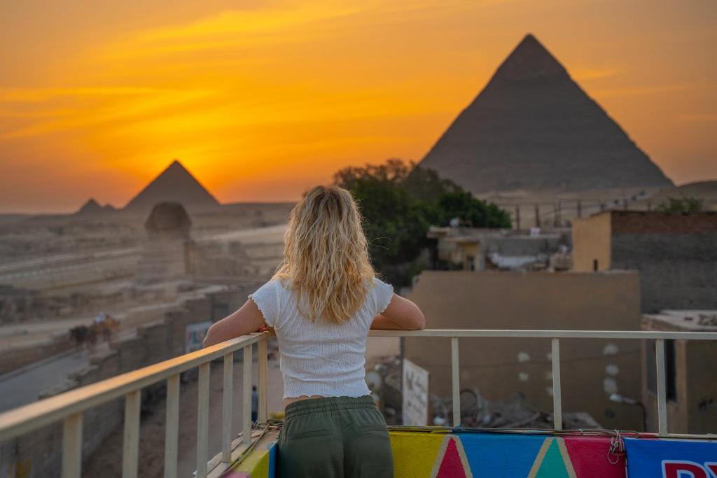Una donna in piedi su un balcone che guarda le piramidi di Pyramids Road Guest House a Il Cairo