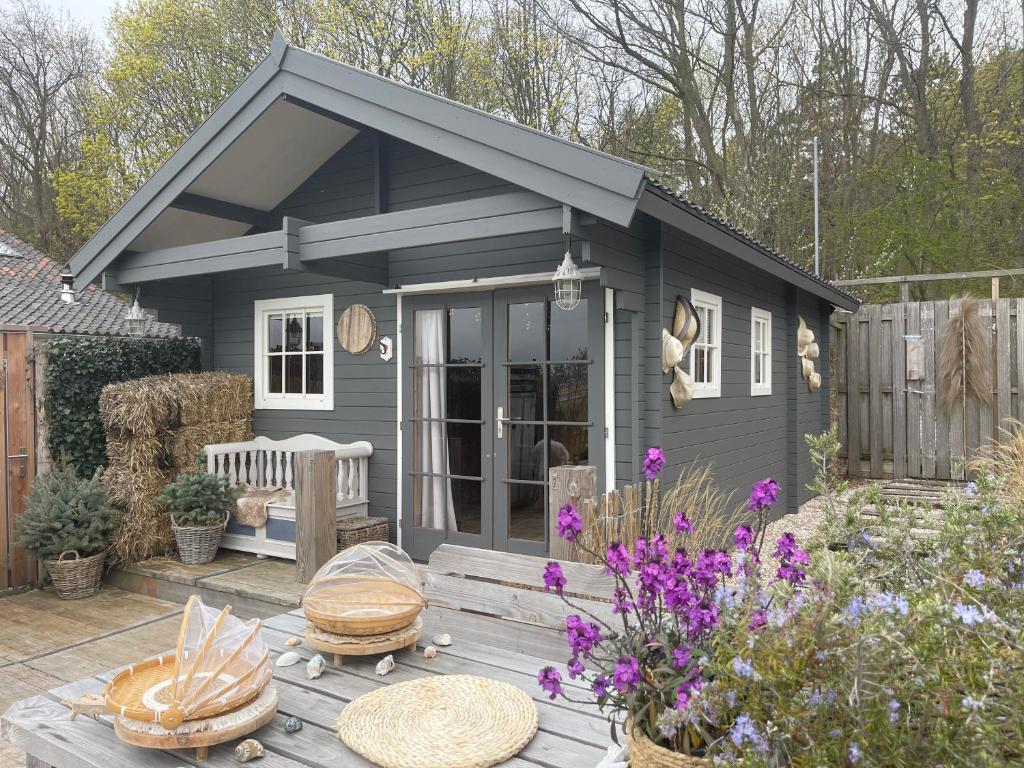 a small grey shed with a picnic table and flowers at Cabin De Duinweg: direct aan duin en bos in Noordwijk